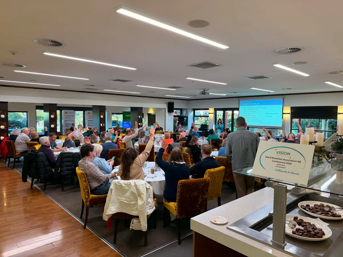 Delegates raising their hands during Blake Harkness's session at the Bed & Breakfast Association NZ Conference 2026 in Christchurch, with the "would I book" website test slide on screen