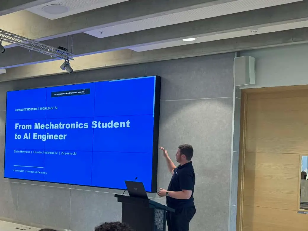 Blake Harkness at the lectern at Graduating into a World of AI at the University of Canterbury, beside his title slide From Mechatronics Student to AI Engineer