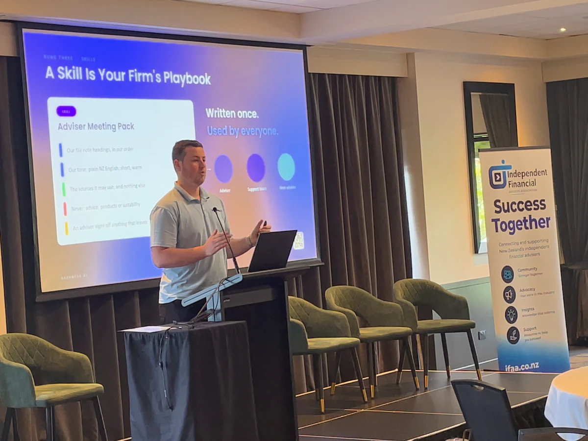 Blake Harkness at the lectern at the IFAA Conference 2026, explaining his slide A Skill Is Your Firm's Playbook beside an Independent Financial Advisers Association banner