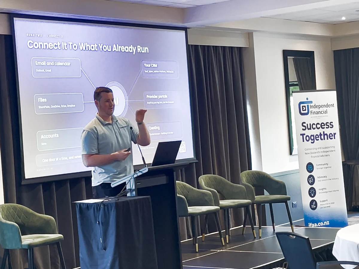 Blake Harkness at the lectern at the IFAA Conference 2026 at Rydges Latimer in Christchurch, beside his slide Connect It To What You Already Run and an Independent Financial Advisers Association banner