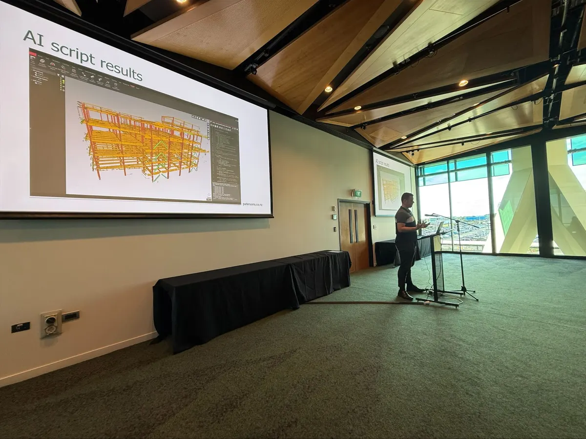 Blake Harkness at the lectern at Survey and Spatial New Zealand in Auckland, with an AI script results slide on the big screen